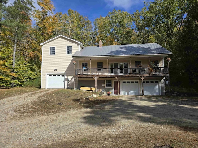 view of front of house featuring a garage, a chimney, metal roof, a porch, and driveway