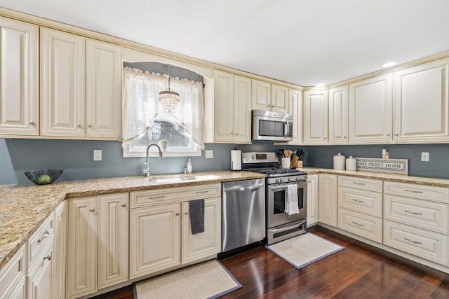 kitchen featuring appliances with stainless steel finishes, cream cabinets, a sink, light stone counters, and dark wood-style floors