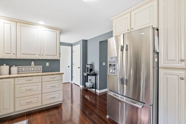 kitchen with stainless steel fridge, dark wood finished floors, light stone counters, and cream cabinetry