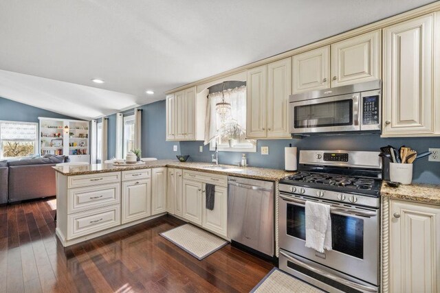 kitchen featuring dark wood-style flooring, cream cabinets, vaulted ceiling, and stainless steel appliances