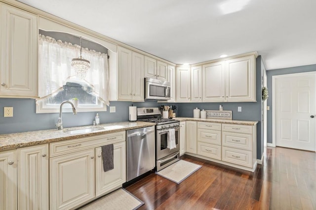 kitchen with a sink, appliances with stainless steel finishes, cream cabinets, and dark wood-style flooring