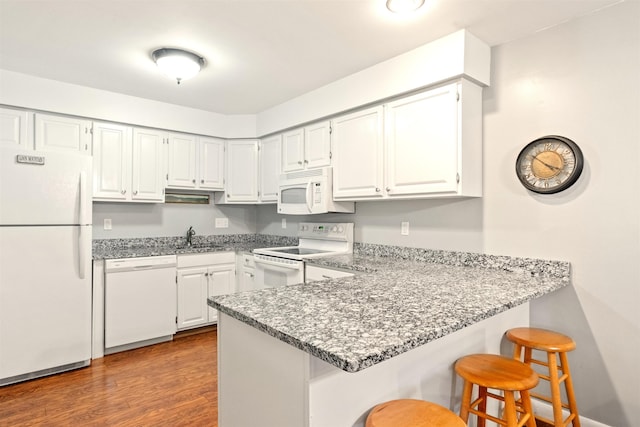 kitchen featuring dark wood-style flooring, a sink, white cabinets, a peninsula, and white appliances