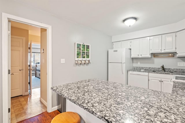kitchen with a peninsula, white appliances, stone countertops, white cabinets, and a sink