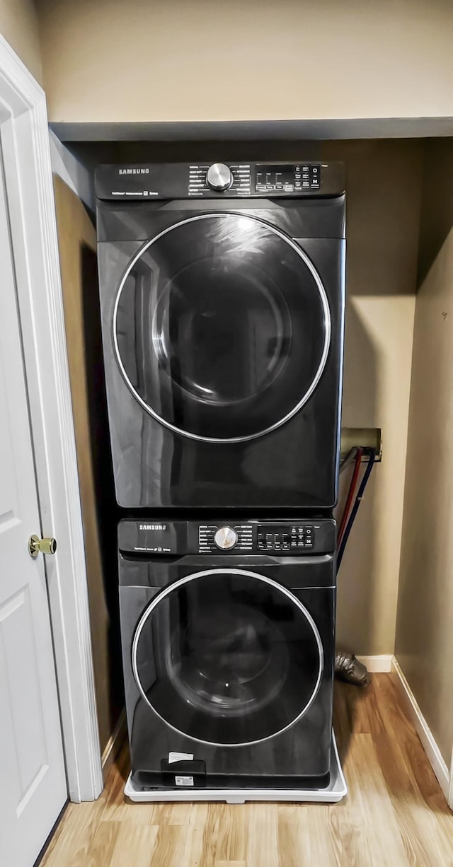 laundry room with laundry area, baseboards, stacked washing maching and dryer, and wood finished floors