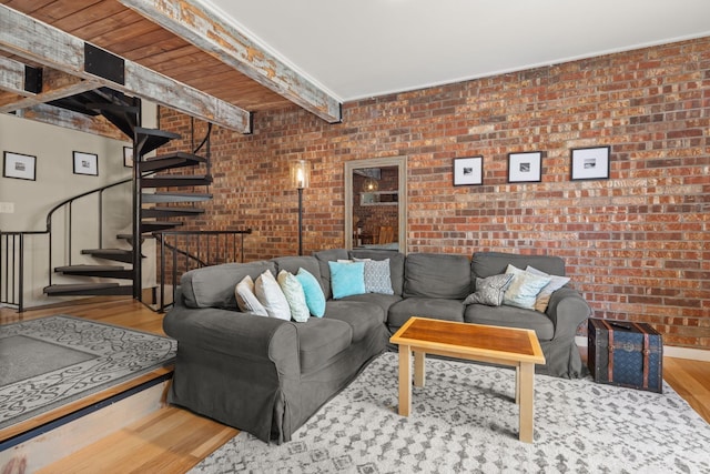 living area featuring wood finished floors, brick wall, stairway, and beamed ceiling