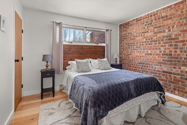 bedroom featuring baseboards, wood finished floors, and brick wall