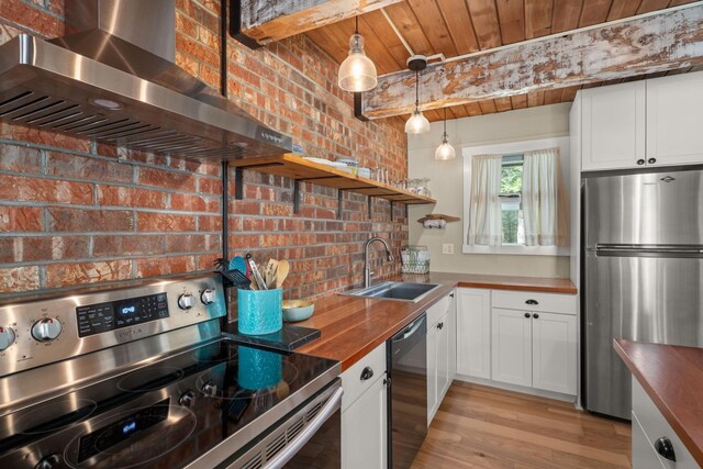 kitchen with wall chimney range hood, appliances with stainless steel finishes, open shelves, a sink, and butcher block countertops