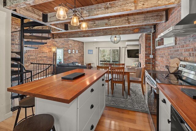 kitchen featuring brick wall, light wood-style floors, wall chimney exhaust hood, wood counters, and stainless steel range with electric cooktop