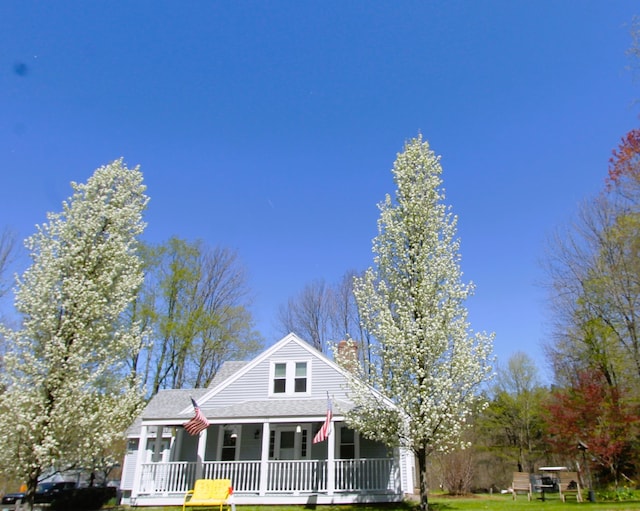 view of front of property with a porch, a shingled roof, a front lawn, and a chimney