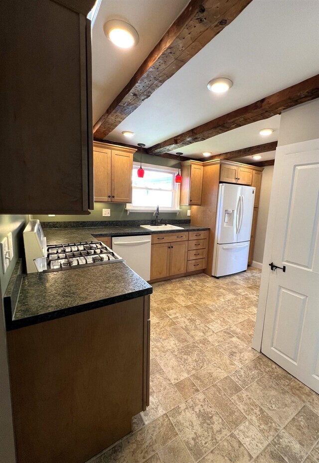 kitchen featuring dark countertops, a sink, beam ceiling, white appliances, and stone finish floor