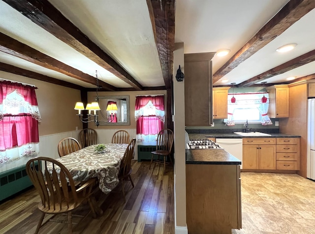 kitchen with white dishwasher, dark countertops, stainless steel gas cooktop, beam ceiling, and a sink