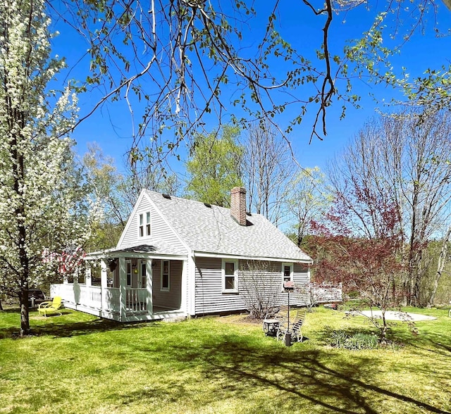 back of property with a lawn, roof with shingles, covered porch, and a chimney