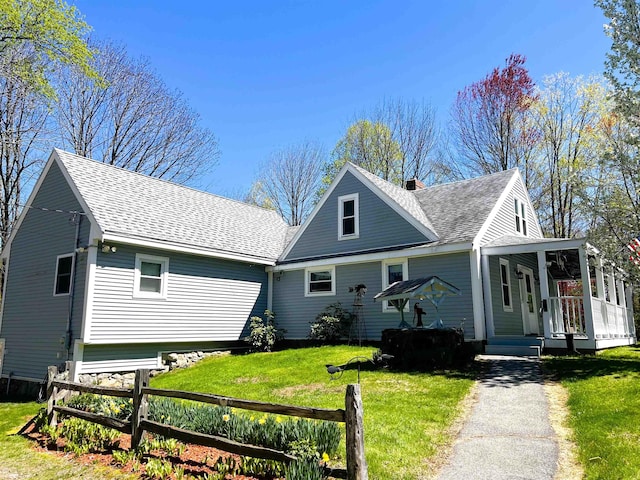 view of front facade with a porch, a shingled roof, fence, and a front yard