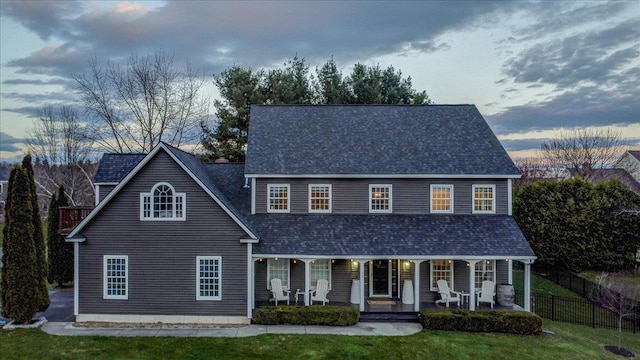 view of front facade featuring a porch, fence, a shingled roof, and a front lawn