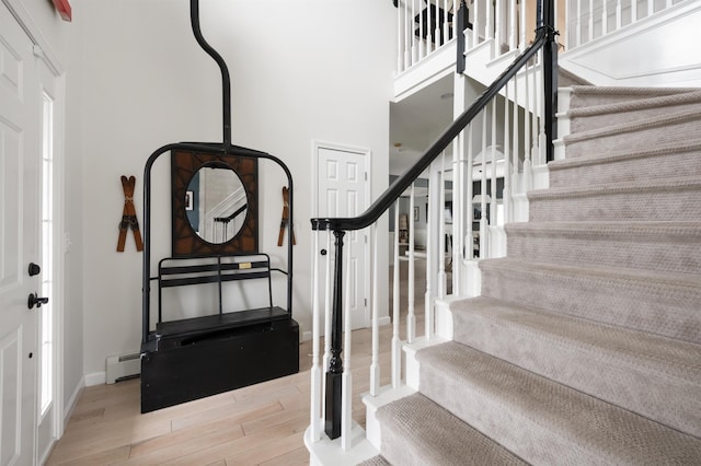 stairs featuring baseboards, a baseboard radiator, wood finished floors, and a towering ceiling