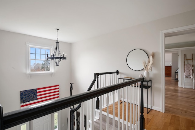 hallway with an inviting chandelier, light wood-style flooring, baseboards, and an upstairs landing