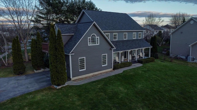 traditional home featuring a front lawn, roof with shingles, central air condition unit, and covered porch