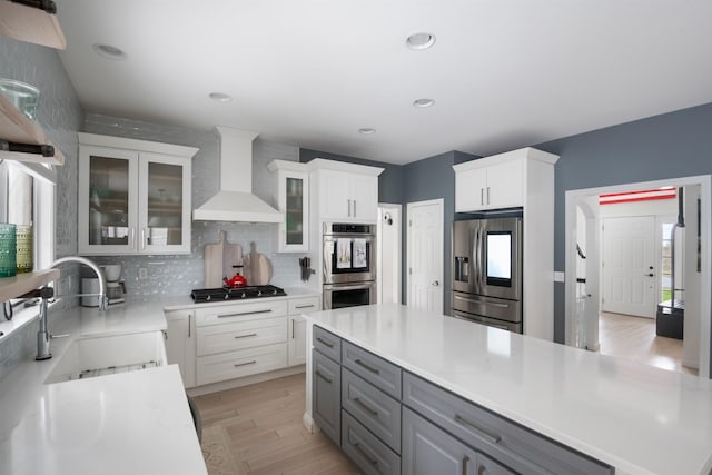 kitchen with wall chimney exhaust hood, tasteful backsplash, a sink, appliances with stainless steel finishes, and gray cabinetry