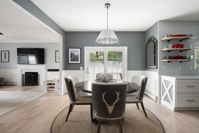 dining space featuring baseboard heating, a wainscoted wall, a fireplace, and light wood finished floors