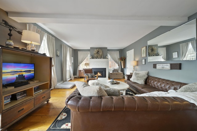 living area featuring a fireplace, beamed ceiling, light wood-style flooring, and a wealth of natural light