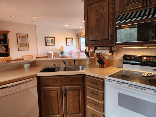 kitchen with dark brown cabinets, a sink, white appliances, light countertops, and recessed lighting