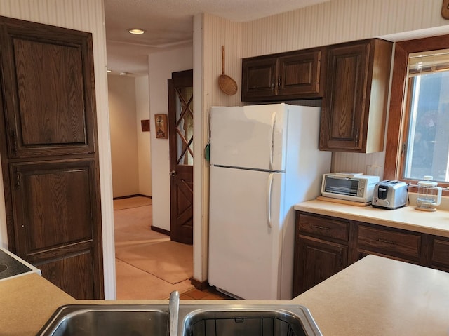kitchen featuring dark brown cabinetry, a toaster, light countertops, a sink, and freestanding refrigerator