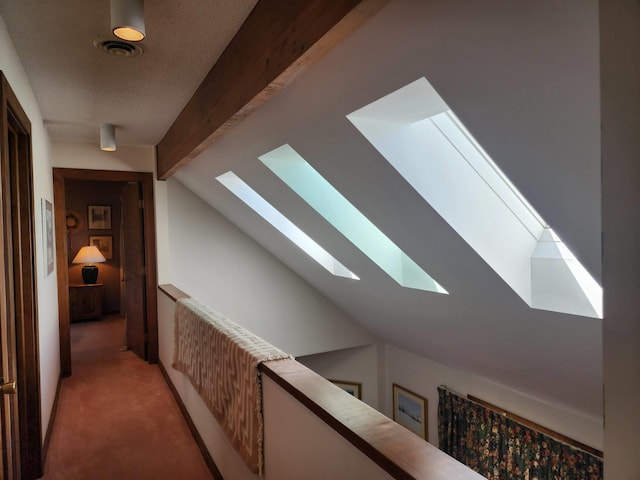 hall with visible vents, carpet flooring, vaulted ceiling with skylight, and an upstairs landing