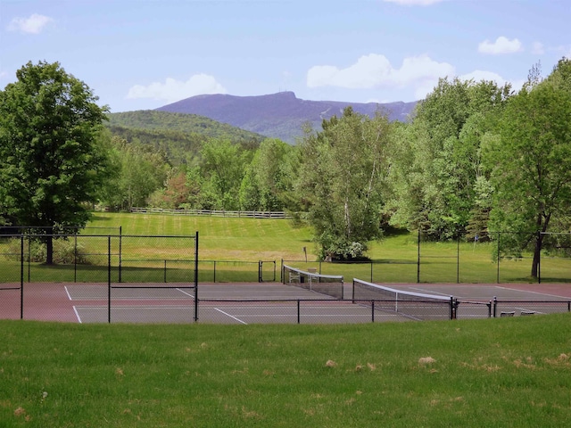 view of tennis court featuring a lawn, fence, and a mountain view