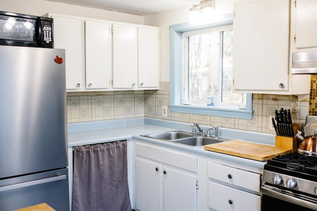 kitchen with appliances with stainless steel finishes, a sink, light countertops, white cabinets, and under cabinet range hood