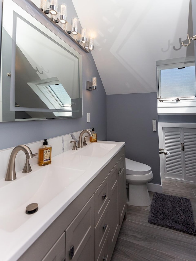 bathroom with double vanity, toilet, a sink, and lofted ceiling