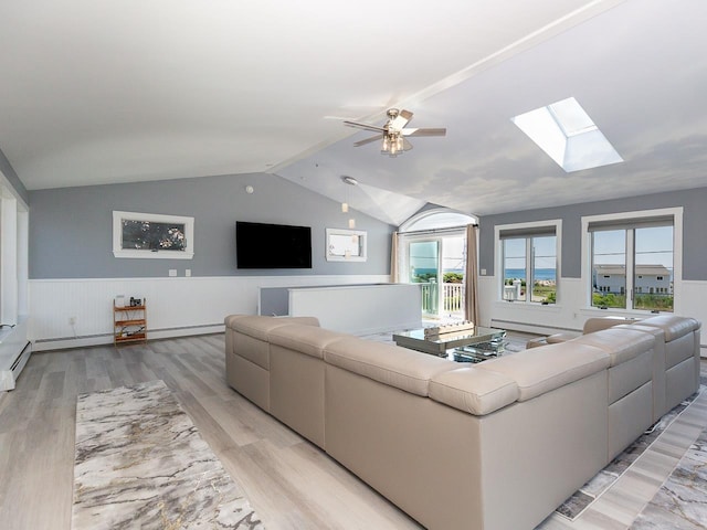 living area featuring a wainscoted wall, ceiling fan, light wood-type flooring, and lofted ceiling with skylight
