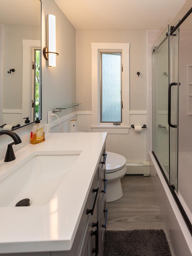full bathroom with shower / bath combination with glass door, vanity, toilet, a wainscoted wall, and a baseboard radiator