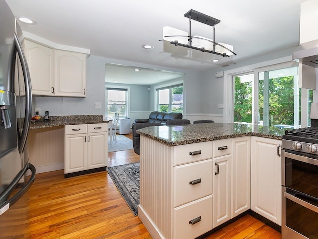 kitchen with white cabinets, stainless steel appliances, light wood-style flooring, and dark stone counters