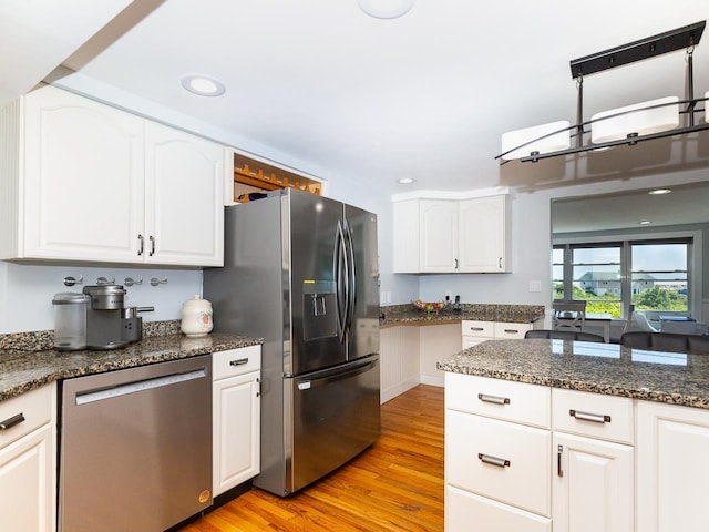 kitchen featuring white cabinets, stainless steel appliances, dark stone counters, and light wood-type flooring
