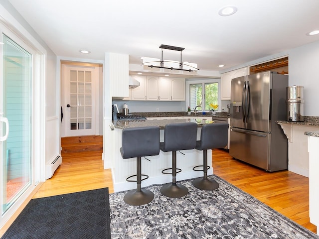 kitchen with a baseboard heating unit, stainless steel fridge, light wood-style flooring, and a breakfast bar