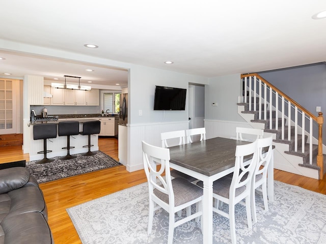 dining space with light wood-style floors, recessed lighting, wainscoting, and stairs
