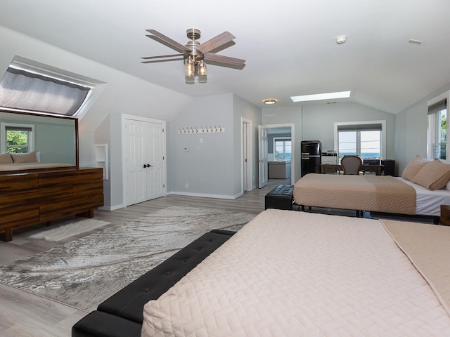 bedroom featuring vaulted ceiling with skylight, baseboards, multiple windows, and light wood finished floors