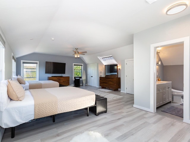 bedroom featuring ceiling fan, a sink, ensuite bath, light wood-style floors, and vaulted ceiling