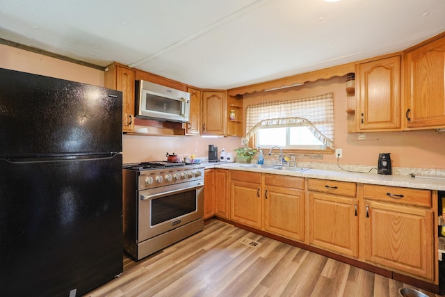 kitchen featuring appliances with stainless steel finishes, open shelves, light wood-type flooring, a sink, and light countertops