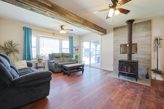 living area with a ceiling fan, beam ceiling, a wealth of natural light, and a wood stove