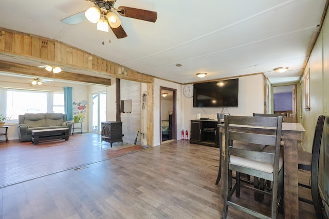 dining area with a wood stove, wood finished floors, wooden walls, a ceiling fan, and vaulted ceiling