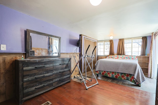 bedroom with wood walls, wood finished floors, and a wainscoted wall