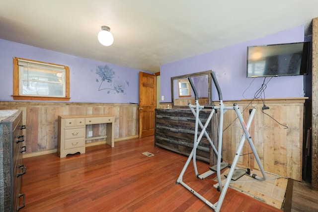 exercise area with wooden walls, visible vents, wood finished floors, and a wainscoted wall