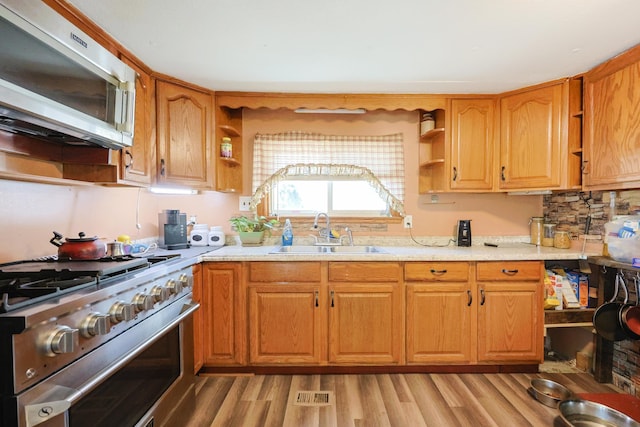 kitchen featuring open shelves, appliances with stainless steel finishes, a sink, light wood finished floors, and light countertops