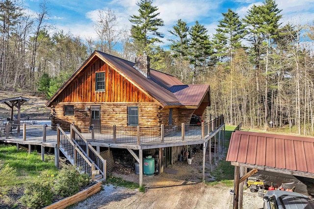 back of house featuring a chimney, log exterior, a deck, and metal roof