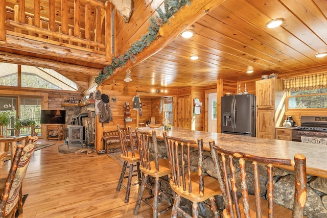 dining room featuring plenty of natural light, a wood stove, wood ceiling, and wooden walls