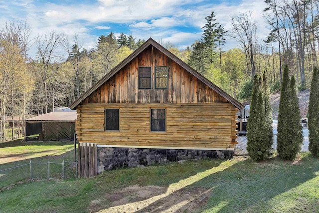 view of side of home with fence, log exterior, a yard, and a wooded view
