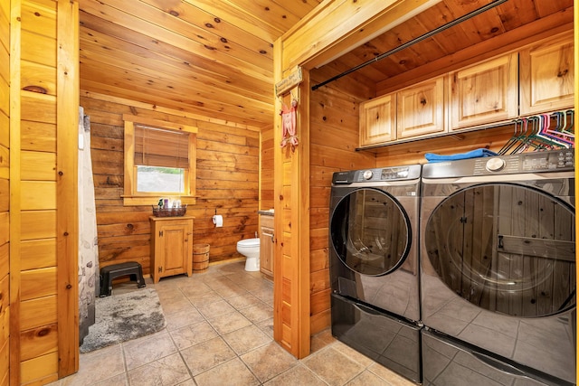 clothes washing area with washing machine and clothes dryer, wooden walls, cabinet space, light tile patterned floors, and wood ceiling