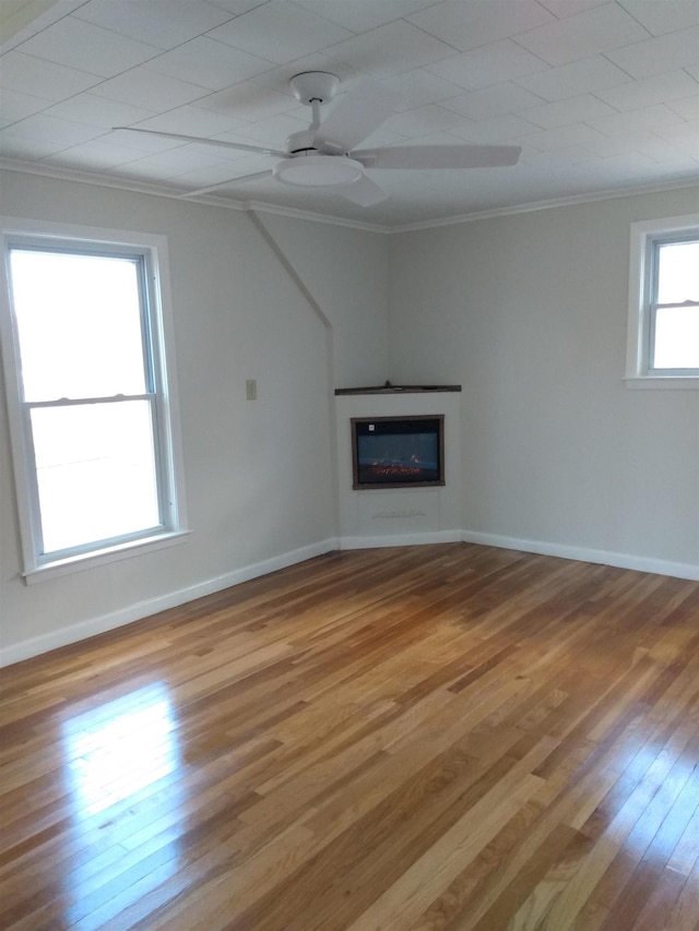 unfurnished living room with crown molding, ceiling fan, light wood-style floors, a glass covered fireplace, and baseboards