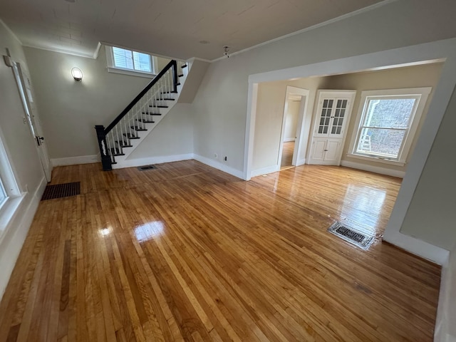 unfurnished living room featuring crown molding, hardwood / wood-style floors, baseboards, visible vents, and stairway